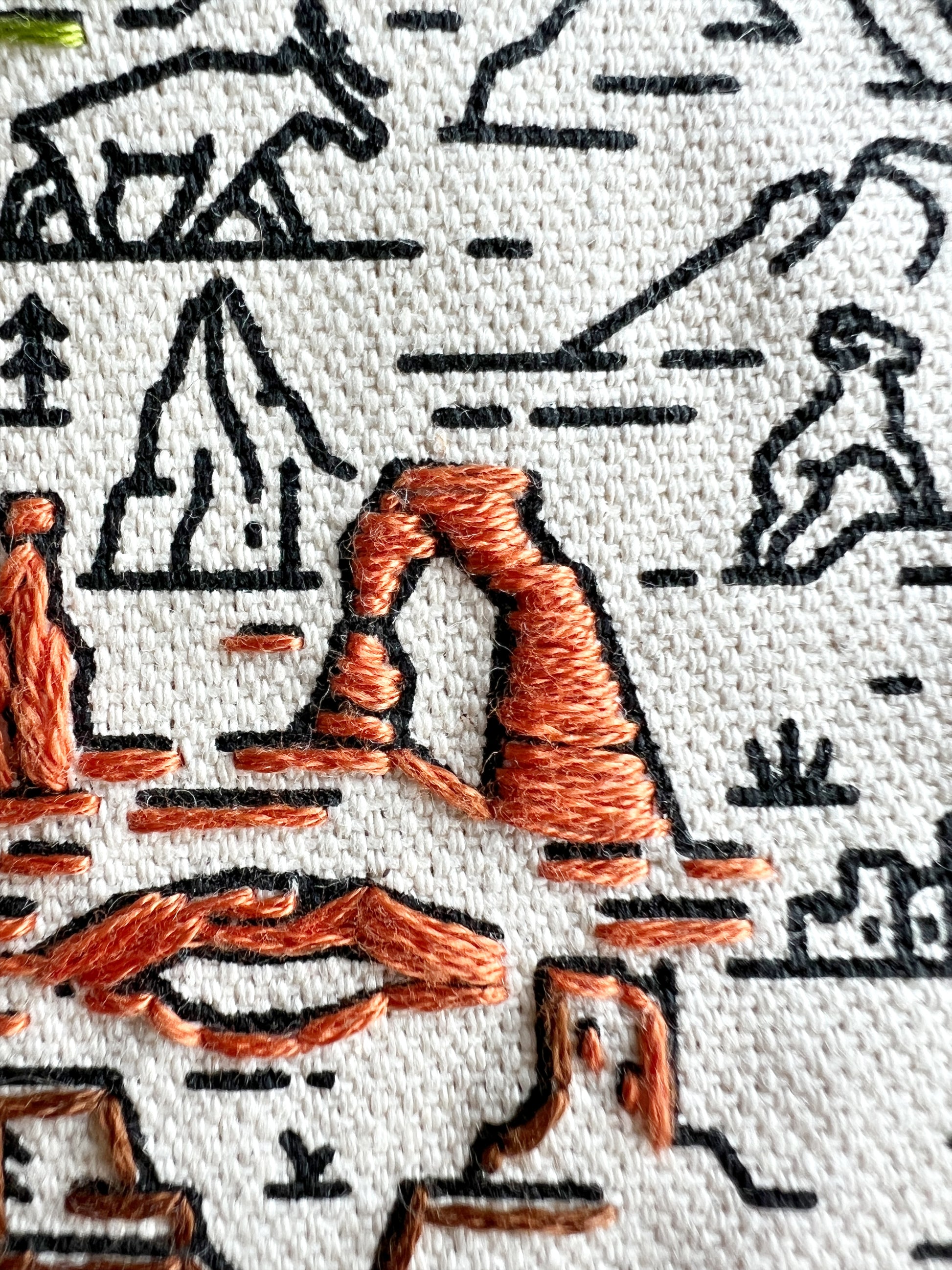 Close up detail of stitches in brown on cream canvas with black screen printed design.  Stitches highlight Arches National Park.