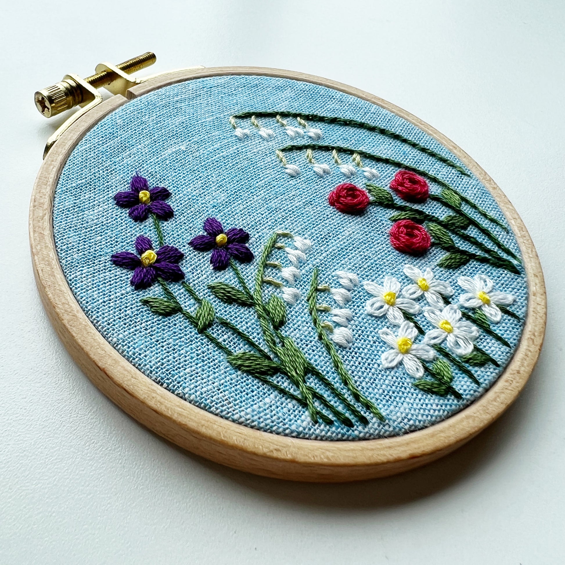 Choose your own adventure for your flower garden.   Hoop shows  Lily of the Valley, Roses, Daisy and violets on  a blue background.
