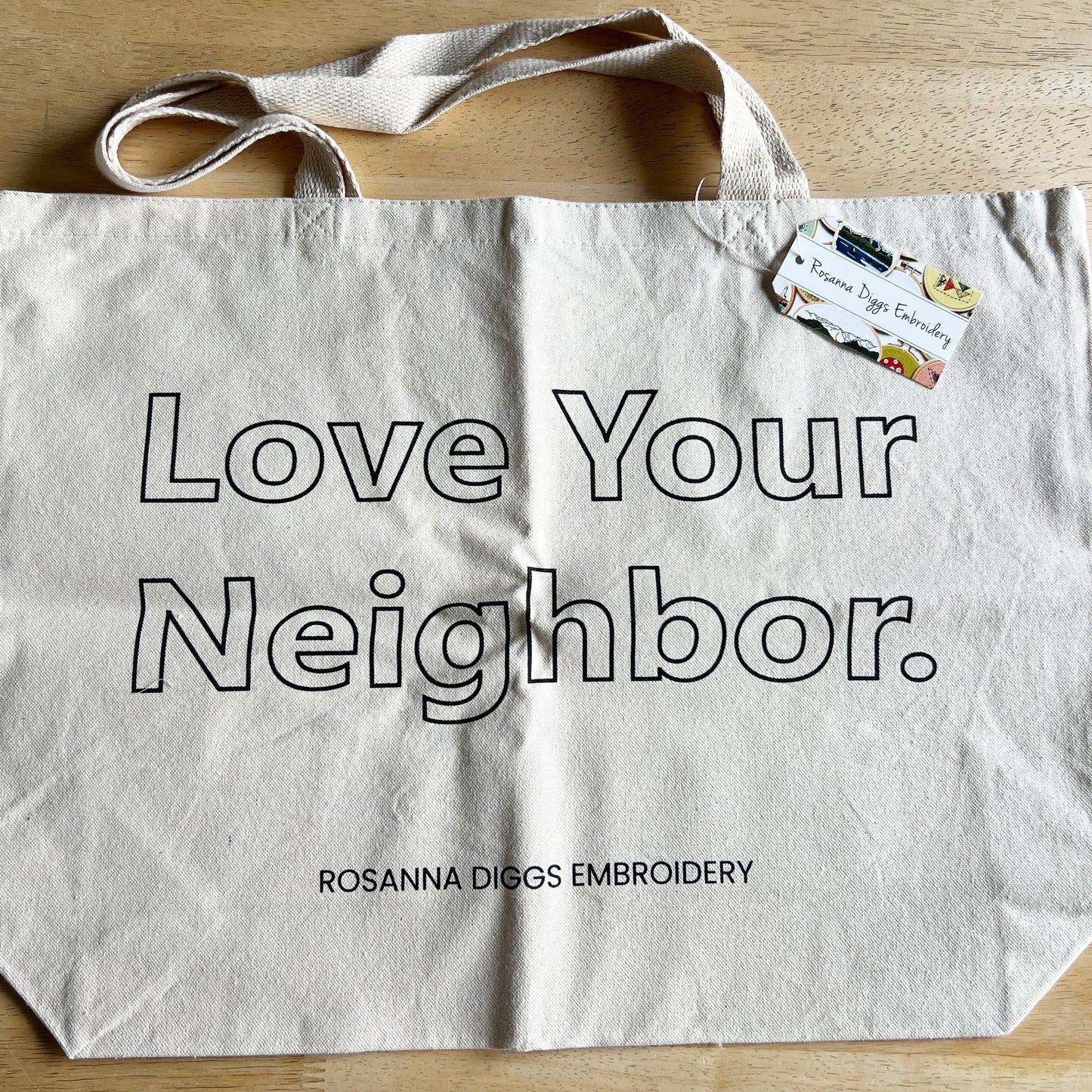 Love Your Neighbor tote is available without the kit. Cream cotton with large open block letters with the words Love Your Neighbor. Rosanna Diggs Embroidery is in small capital letters at the bottom edge of bag.