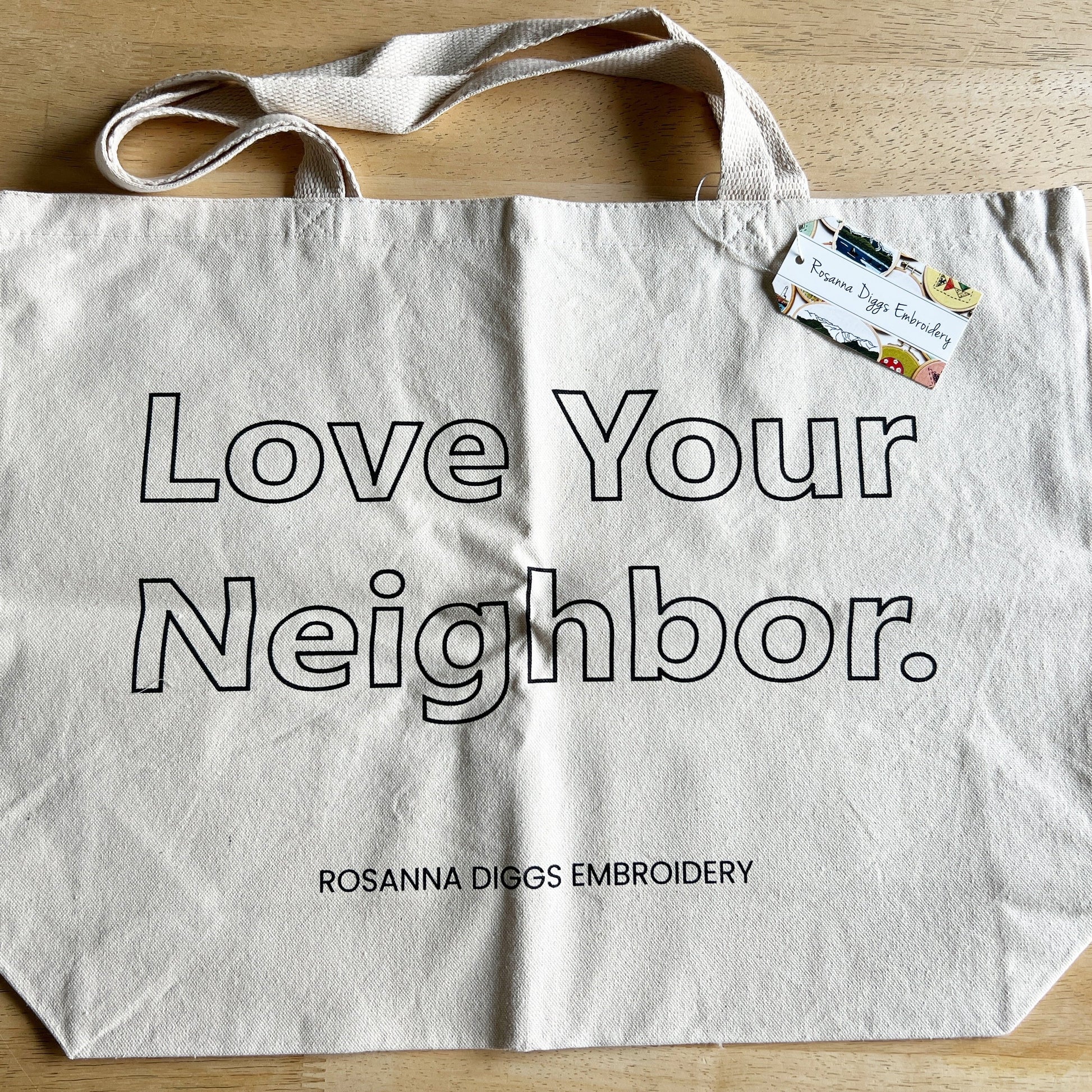 Love Your Neighbor tote is available without the kit. Cream cotton with large open block letters with the words Love Your Neighbor.  Rosanna Diggs Embroidery is in small capital letters at the bottom edge of bag.