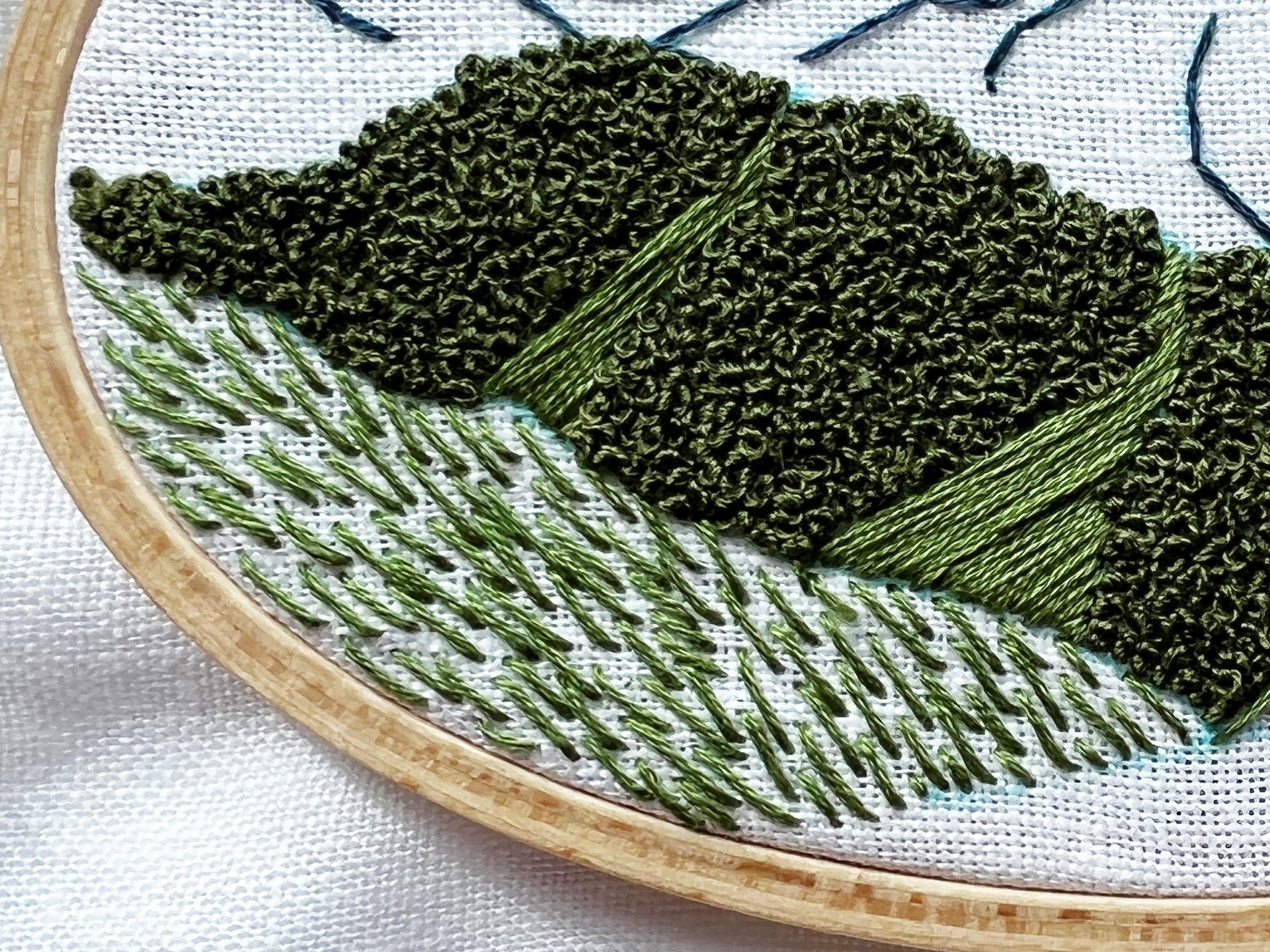 Close up of foreground development of Hurricane Ridge Embroidery.  Using traced lines from pattern trees and hillsides have been completed while grass has been started.