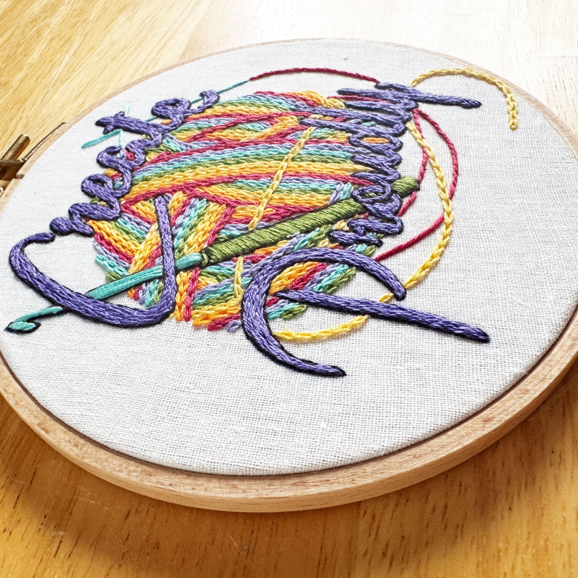 Embroidery hoop with colorful thread design on a wooden surface
