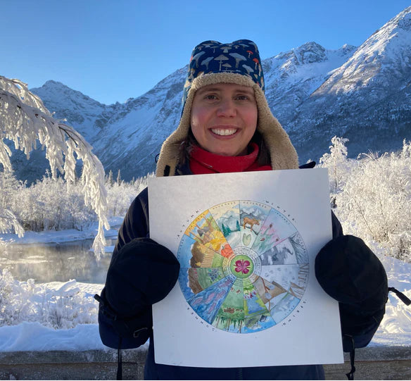 Person holding a colorful circular artwork in a snowy mountain landscape