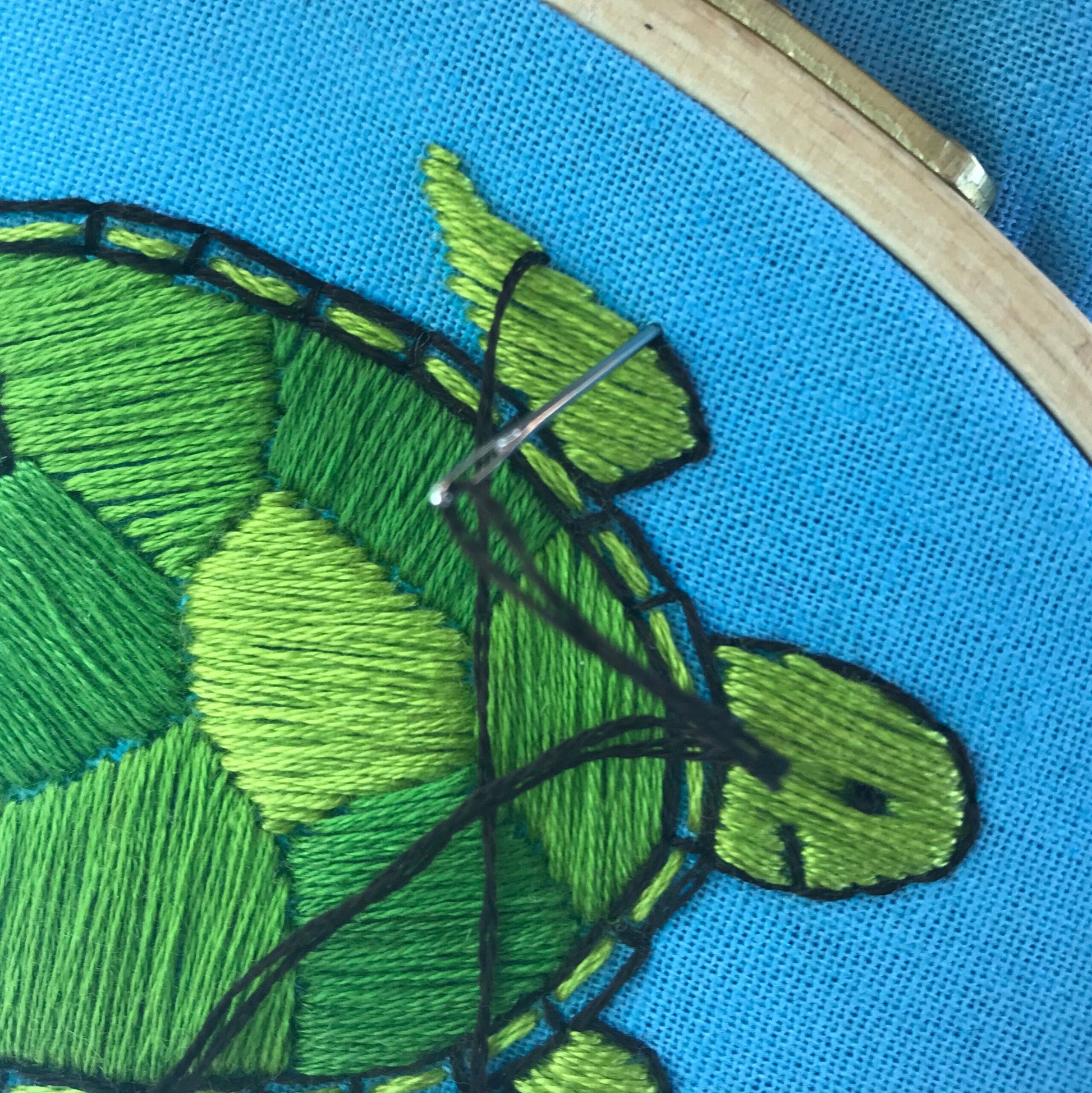 Close up of stitch detail in Green Sea Turtle hand embroidery.  Green turtle is being outlined in black thread with needle ready to pull through next stitch.