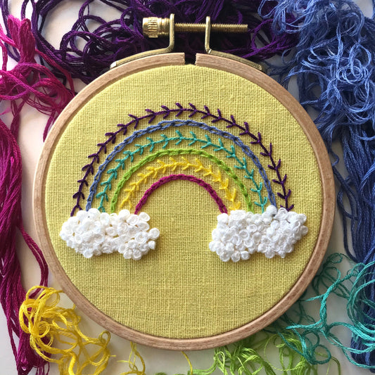 Radiant Rainbow PDF.  This pattern teaches different stitches resulting in a modern rainbow with puffy clouds below a 6 banded rainbow.