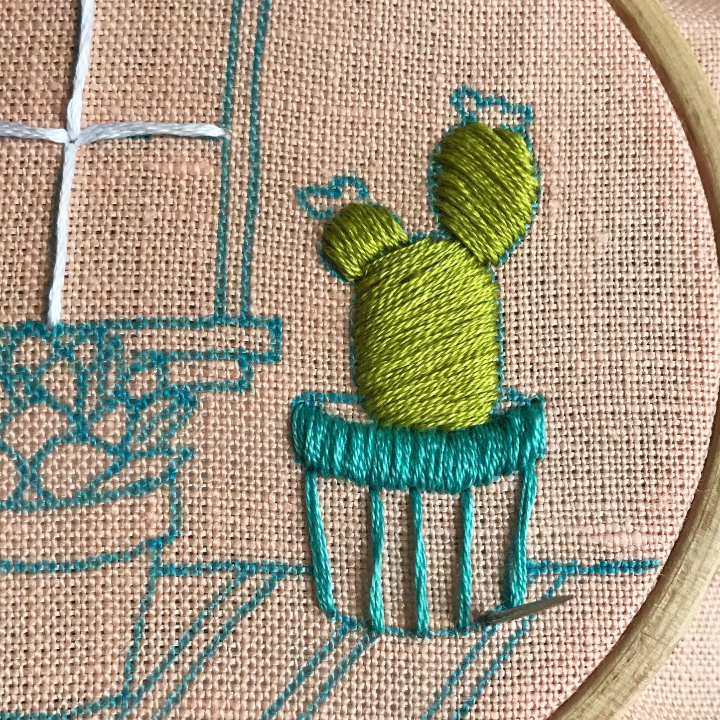 Stitch detail of larger cactus in Cozy Cactus PDF. Stitching is in progress with needle poking up through linen fabric.