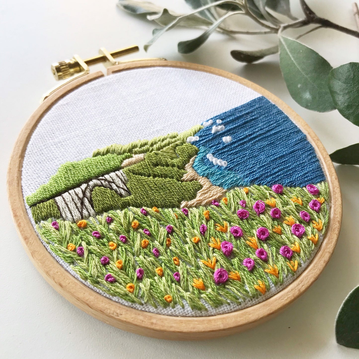 Big Sur California Hand Embroidery PDF. 13 page booklet gives easy to follow directions to complete this oceanside Modern Embroidery. Flowers in the foreground with HWY 101 Big Sur Bridge in the background. White waves crashing on beach.