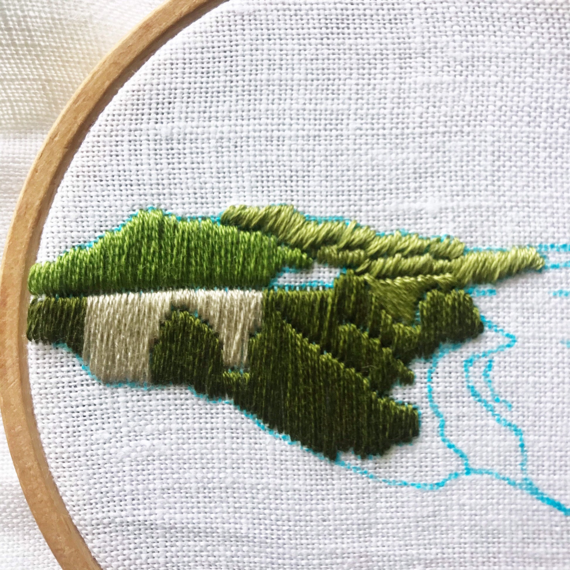 Close up of stitches in Big Sur California Hand Embroidery.  Base color of green is complete for the hills as well as brown for bridge.  Blue marker denotes next stitches.