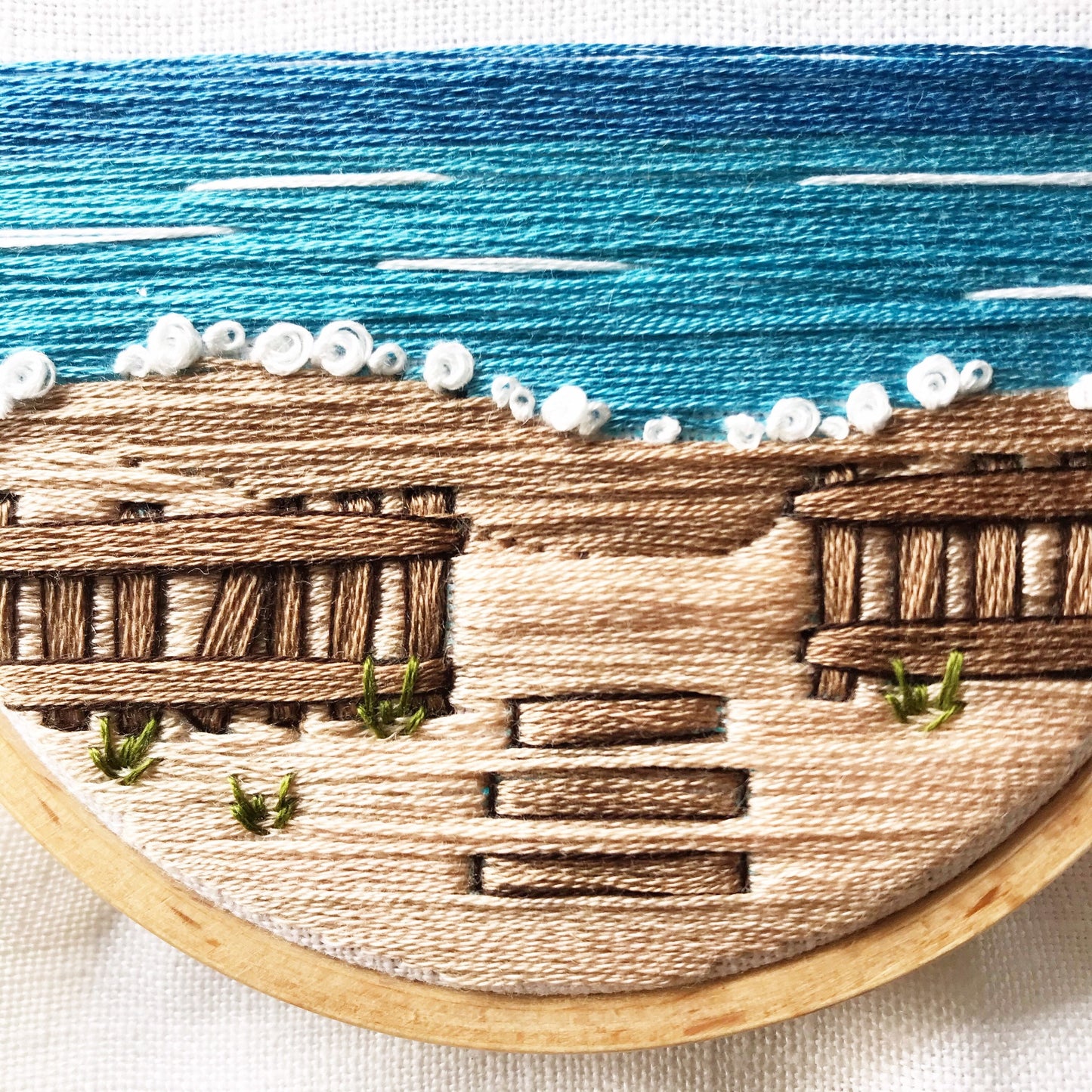 Close up details of A Day at the Beach Modern Embroidery PDF. White caps of waves border between ocean and sand with rustic wooden fence.