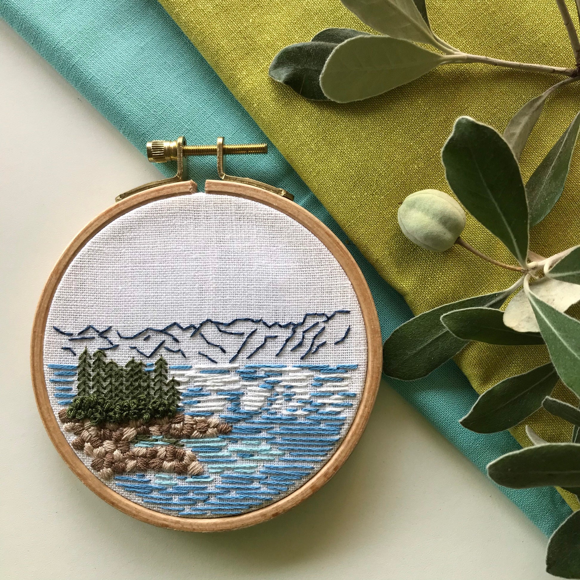 Lake Tahoe is a great pattern to DIY your own modern embroidery hoop art. This 12 page pdf details everything you need to know to stitch this beautiful embroidery.  Mountains in the background with trees, rocks and lake in front.