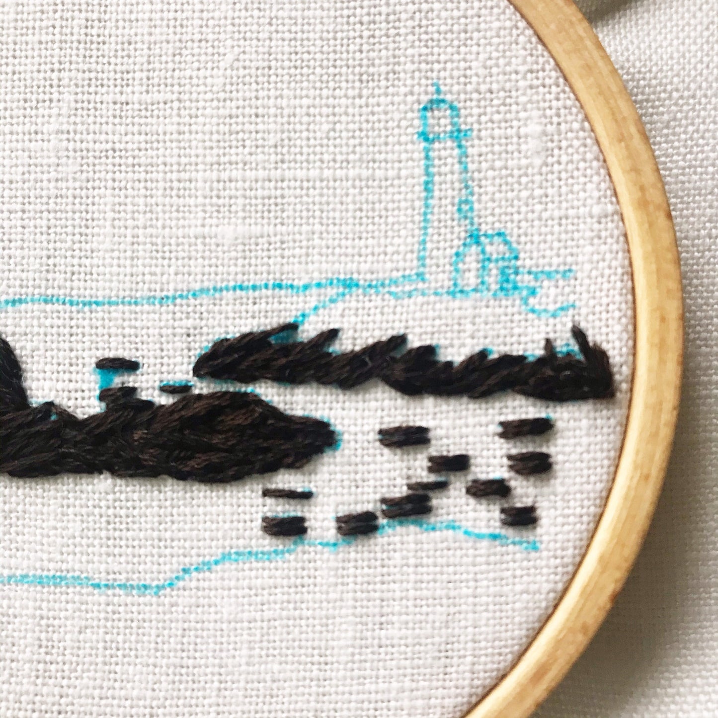 Lighthouse by the Bay Hand Embroidery in progress. Blue marker outlines stitch design. Some dark stitches for rocks have been completed.