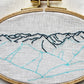 Hurricane Ridge Embroidery in progress.  Far mountains have been outlined in floss.  Remaining features have been traced with a water soluble blue marker on linen to show next steps.