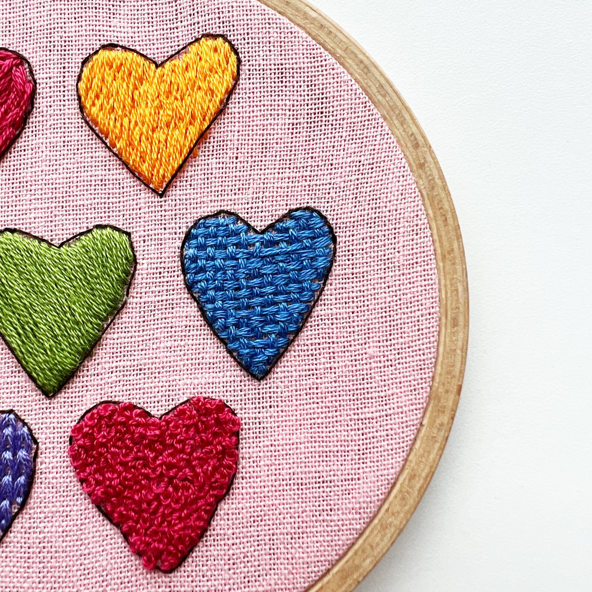 Close up of I Heart Stitching Complete Beginner Embroidery Kit.  Hearts in yellow, green, blue and red show four different stitch types.