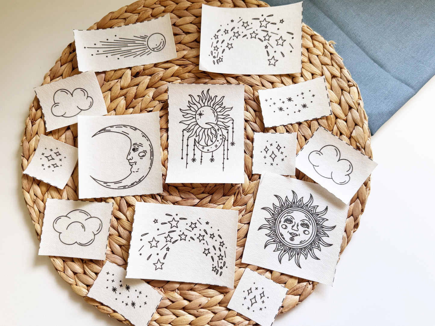 A collection of stick and stitch designs printed with black celestial illustrations like suns, moons, stars, and constellations, arranged on a round woven straw mat.