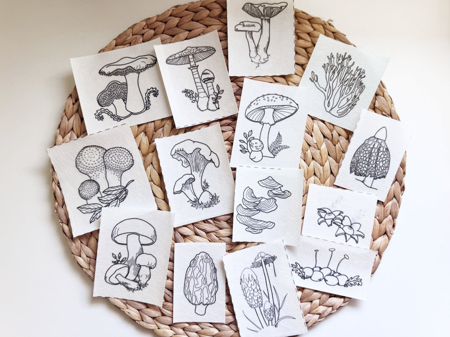 A collection of stick and stitch designs with black line drawings of mushrooms and botanical illustrations, arranged on a round woven straw mat against a plain light background.